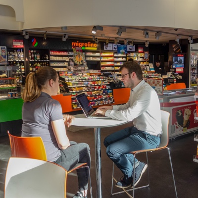 Intervistatore seduto al tavolo di una stazione di servizio a Zurigo che parla con un utente dell'applicazione POS retail